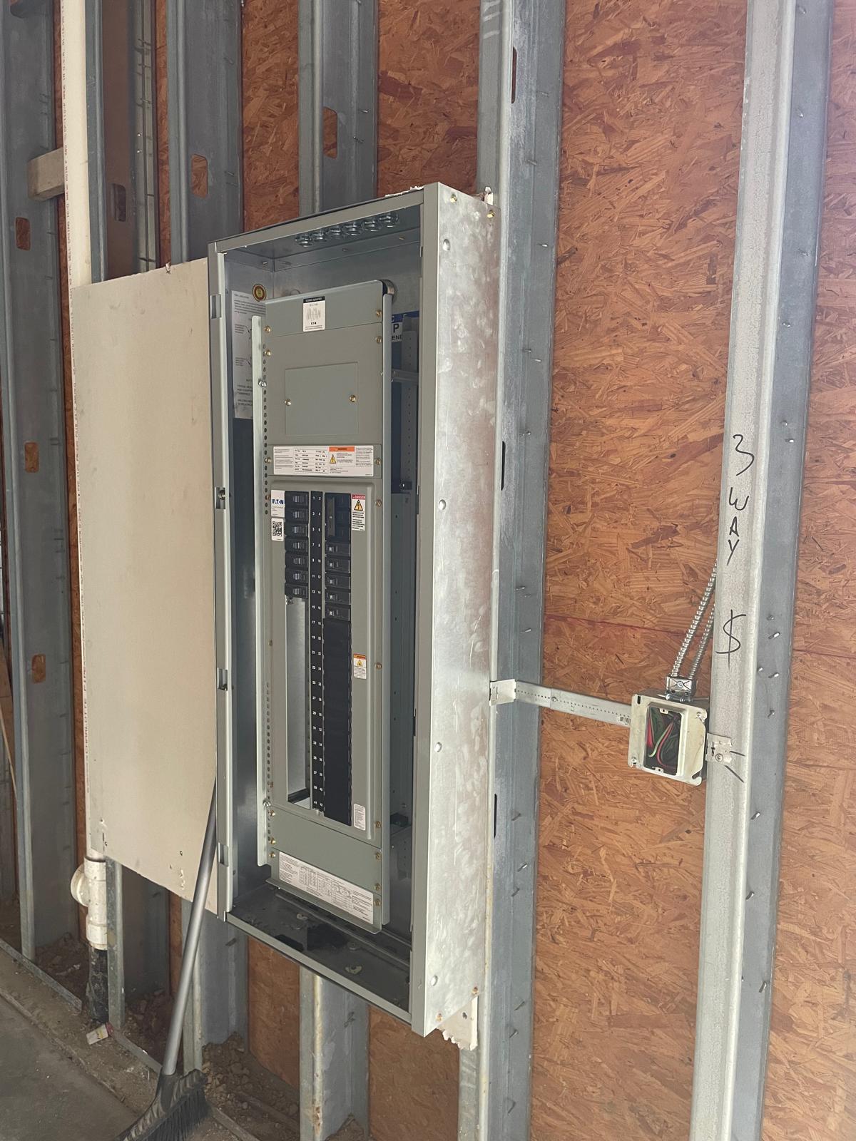 Brightway Electric technician working inside an open electrical panel during construction